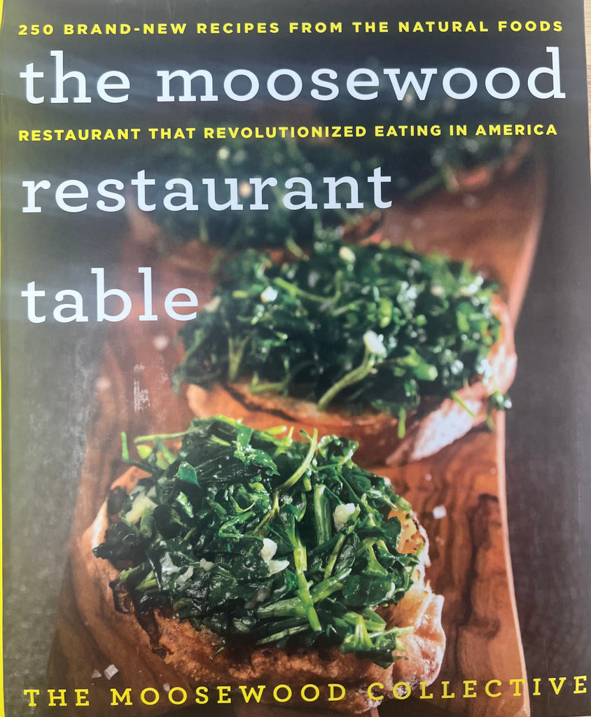 Book cover of 'The Moosewood Restaurant Table' with green leafy vegetables on a wooden board.